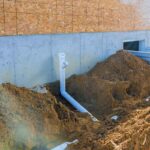 cadru de aproape cu teava din PVC langa o casa sugerand instalarea canalizarii spre o fosa septica